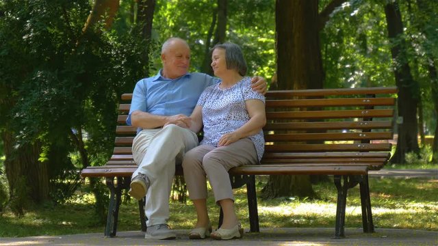 Senior couple talking while sitting on bench in summer park. 4k