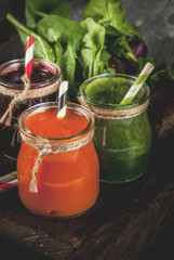 Vegan diet food. Detox drinks. Freshly squeezed juices and smoothies from vegetables: beets, carrots, spinach, cucumber, apple. On dark stone background, wooden tray, ingredients.