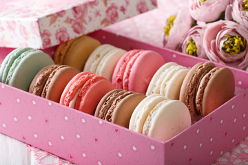 French macaroons in a pink box and flowers close-up. horizontal