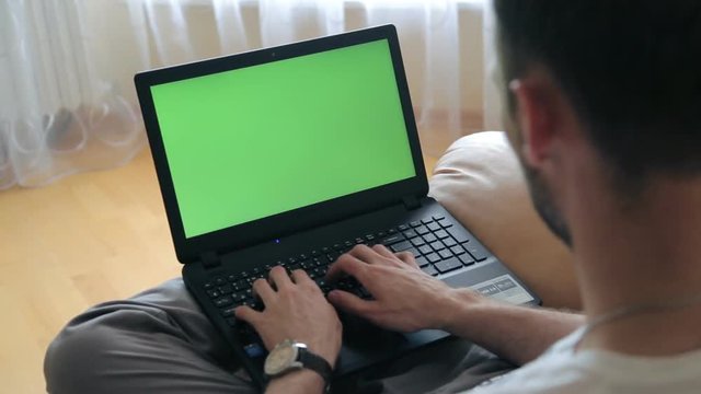 A man uses a laptop in his home office. Green screen for your custom screen content