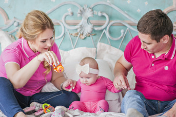 Mom and Dad play with their beautiful daughter on the bed