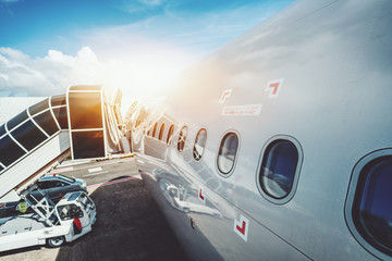 Wide angle shooting of contemporary white airplane body with numerous windows and boarding ramp staying on maintenance in airport of Male on sunny day with staff car near it