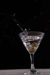 Vodka splashing in martini glass with olives