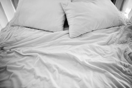 Crumpled white sheets and pillows on the bed in the morning. Double bedroom, kept warm flesh. Background white creased cloth. The texture of the fabric after sleep.