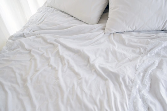 Crumpled white sheets and pillows in the morning. Bed for two, preserved the warmth of the flesh. Background white creased cloth. The texture of the fabric after sleep.