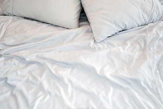 Crumpled white sheets and pillows. Morning bed kept warmly bodies. Background white creased cloth. The texture of the fabric after sleep.