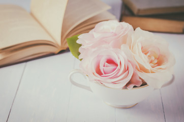 Pink artificial rose flowers at white cup with books