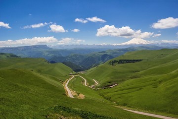 Fototapeta na wymiar Высокая гора Эльбрус, красивый вид на снежные вершины, горная панорама, достопримечательности и горы Северного Кавказа, автотуризм, горная дорога