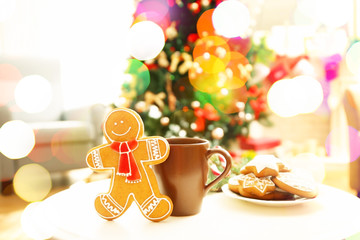 Gingerbread man, cup and plate with cookies on table against blurred background