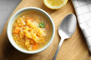 Bowl with tasty lentil dish and spoon on kitchen table, closeup