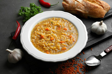 Plate with tasty lentil soup and ingredients on dark table