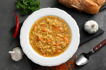 Plate with tasty lentil soup and ingredients on dark table