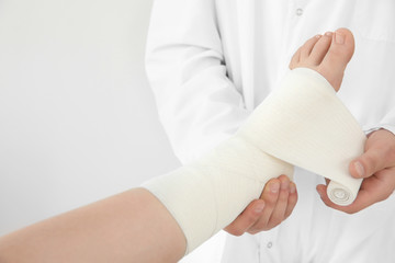 Doctor applying bandage onto patient's leg in clinic, closeup