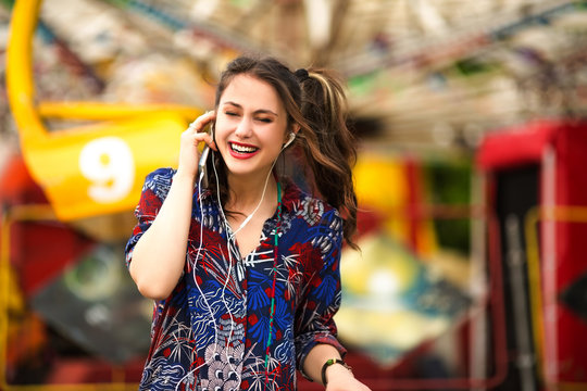 Young woman listening music,smiling and holding smart phone outdoors