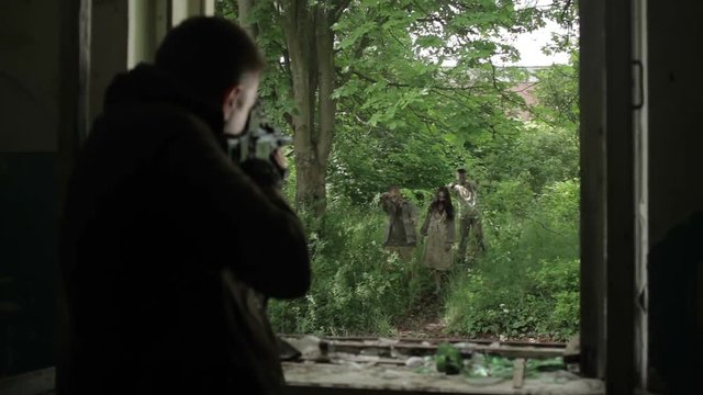 A man shoots zombies from the window of an abandoned house.
