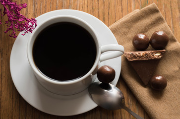 Hot fresh strong black coffee on a saucer next to chocolate and sweet candy