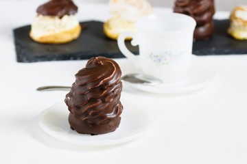 Chocolate coated mousse dessert served on white tablecloth with china teacup and selection plate of other desserts