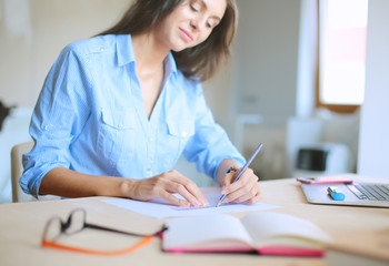 Young woman sitting at the desk with instruments, plan and laptop