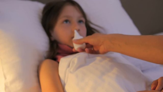 A sick child. A child is ill. A sick girl lies in the bed. The child has a fever. The girl has the flu. Mom treats a sick girl. Nasal spray.