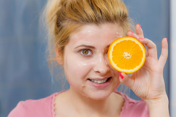 Woman having gel mask on face holding orange