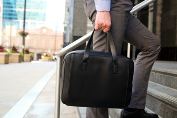 Businessman walking and holding  a  leather briefcase in his handss Modern city behind