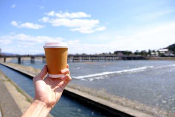 Man holding a cup of coffee with Togetsukyo bridge background