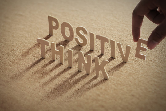 THINK POSITIVE wood word on compressed or corkboard with human's finger at E letter..