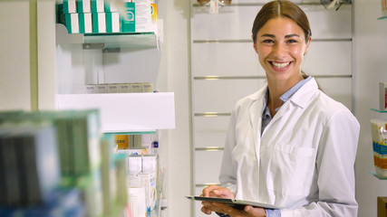 Portrait of a beautiful young girl (woman) pharmacist, consultant, working at a pharmacy, selling and checking medication, smiling, giving advice. Concept: profession, medecine, medical education.