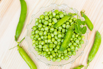 Fresh green peas on a plate. Light wooden background