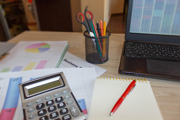 Close up detail view of a white work desk with a laptop computer and a calculator with numbers on the screen.