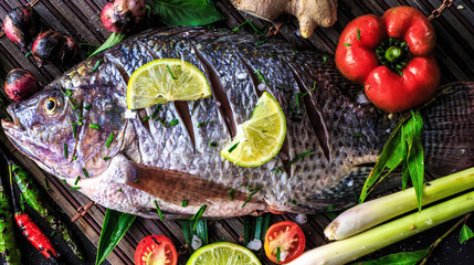 Top view delicious fresh fish and herbs and spices, lemon, tomato, chili and various vegetables on dark wood background, space for texture. Healthy food, diet or cooking concept.