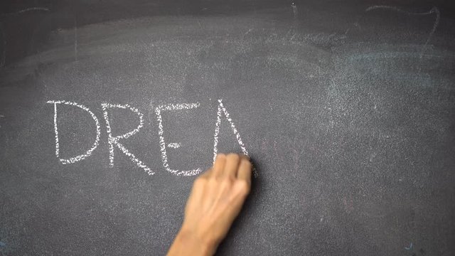 Woman's hand writing "DREAM" with white chalk on blackboard