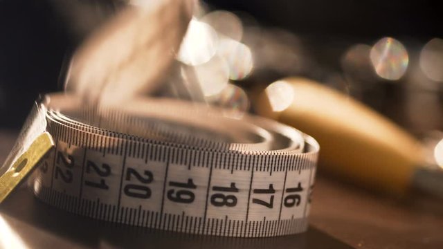 female hand takes metric tape line, which lay on wooden desk full of instruments, materials, equipment for handmade needlework of leather, to take measurements during workshop