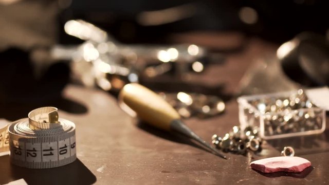 female hand takes metric tape line, which lay on wooden desk full of instruments, materials, equipment for handmade needlework of leather, to take measurements during workshop