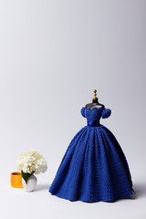 Fashion Concept. Crochet blue ball gown on a mannequin and vase with flowers. Clothes for 11-inch doll. Cover for a magazine