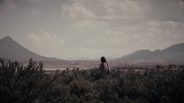 Indigenous woman seated on the bolivian fields wearing a traditional bolivian hat.4k
