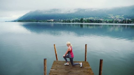 A young woman warms up in a picturesque place. On a wooden pier on the background of a mountain lake and mountains in the Alps, Austria