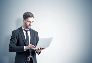 Young businessman with a laptop, gray wall