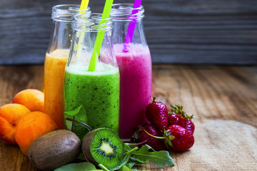 Fresh smoothies in bottles in three colors: green with spinach and kiwi, pink with strawberries, orange with apricots, healthy detox smoothies