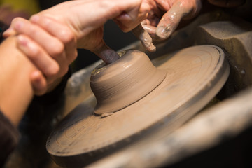 Hands working on a spinning pottery wheel, making pottery out of clay mud. close up photograph with a shallow depth of field.