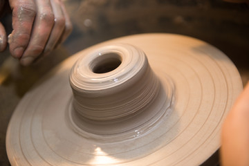Hands working on a spinning pottery wheel, making pottery out of clay mud. close up photograph with a shallow depth of field.
