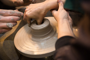Hands working on a spinning pottery wheel, making pottery out of clay mud. close up photograph with a shallow depth of field.