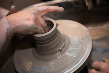 Hands working on a spinning pottery wheel, making pottery out of clay mud. close up photograph with a shallow depth of field.