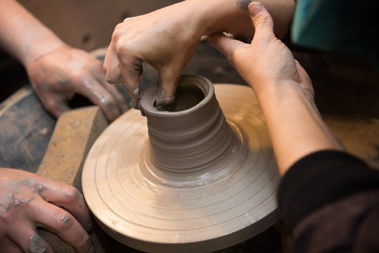 Hands working on a spinning pottery wheel, making pottery out of clay mud. close up photograph with a shallow depth of field.