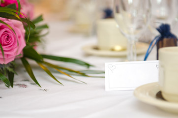 An empty blank paper table card name plate sign on a wedding table, with beautiful pink flowers shot with a shallow depth of field. perfect for placing names in composite designs.