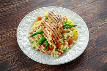 couscous salad with grilled chicken and asparagus on white plate. wooden rustic table. healthy food