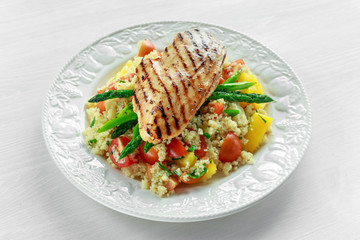 couscous salad with grilled chicken and asparagus on white plate. wooden table. healthy food