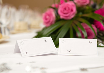 An empty blank paper table card name plate sign on a wedding table, with beautiful pink flowers shot with a shallow depth of field. perfect for placing names in composite designs.