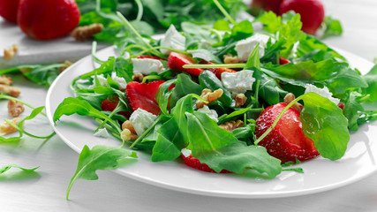 Fresh strawberry salad with feta cheese, arugula on white plate