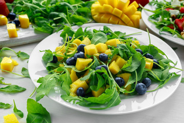 Mango, blueberries salad with arugula on white plate